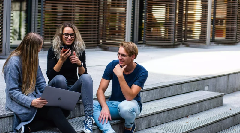 trio de jovens sentados em escadaria de instituição com notebook buscando cursos de inglês baratos para intercâmbio